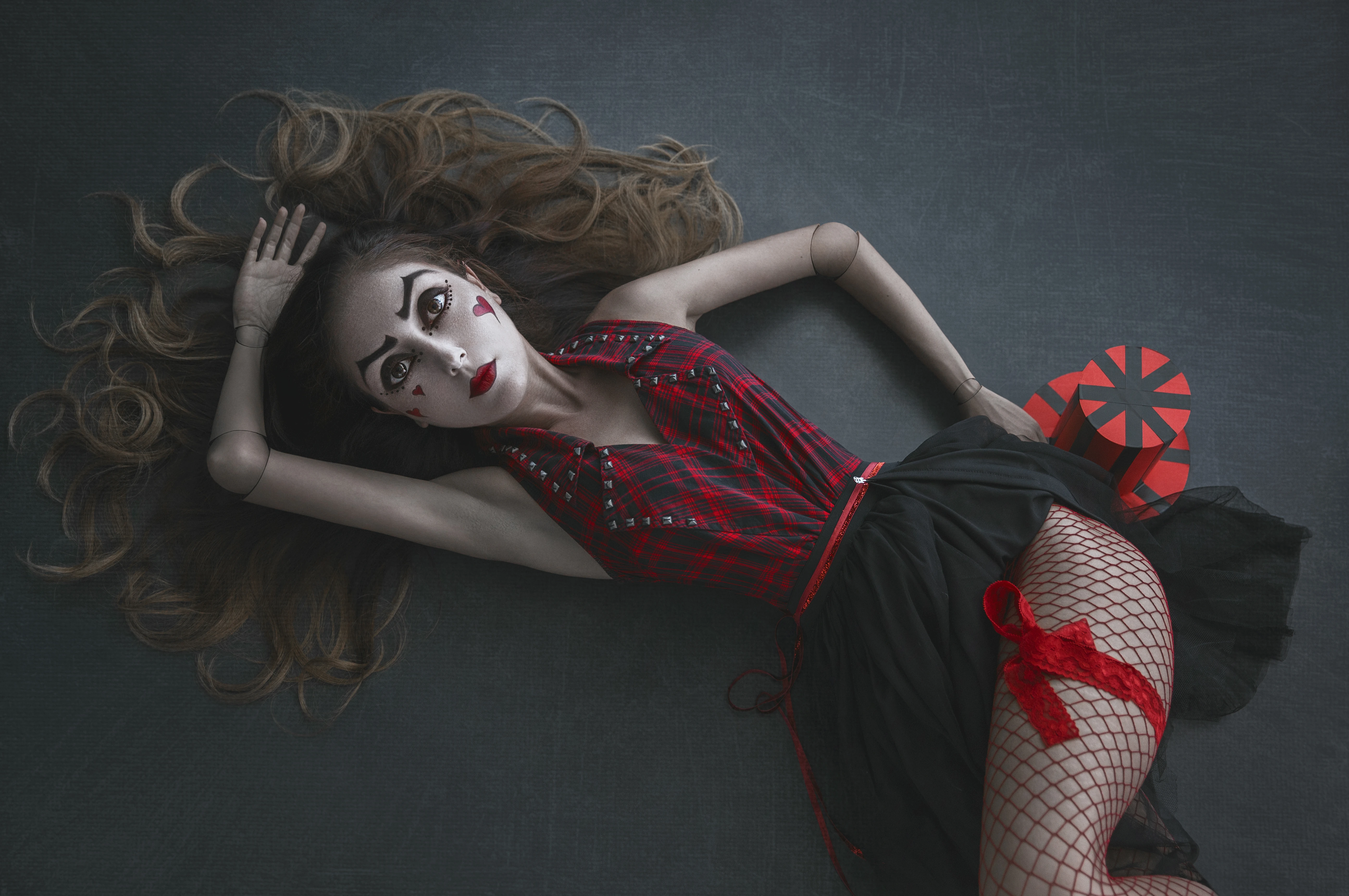 conceptual compositing dreamlike visual narrative of woman styled as a marionette doll, lying on the floor with theatrical makeup and segmented joints.
