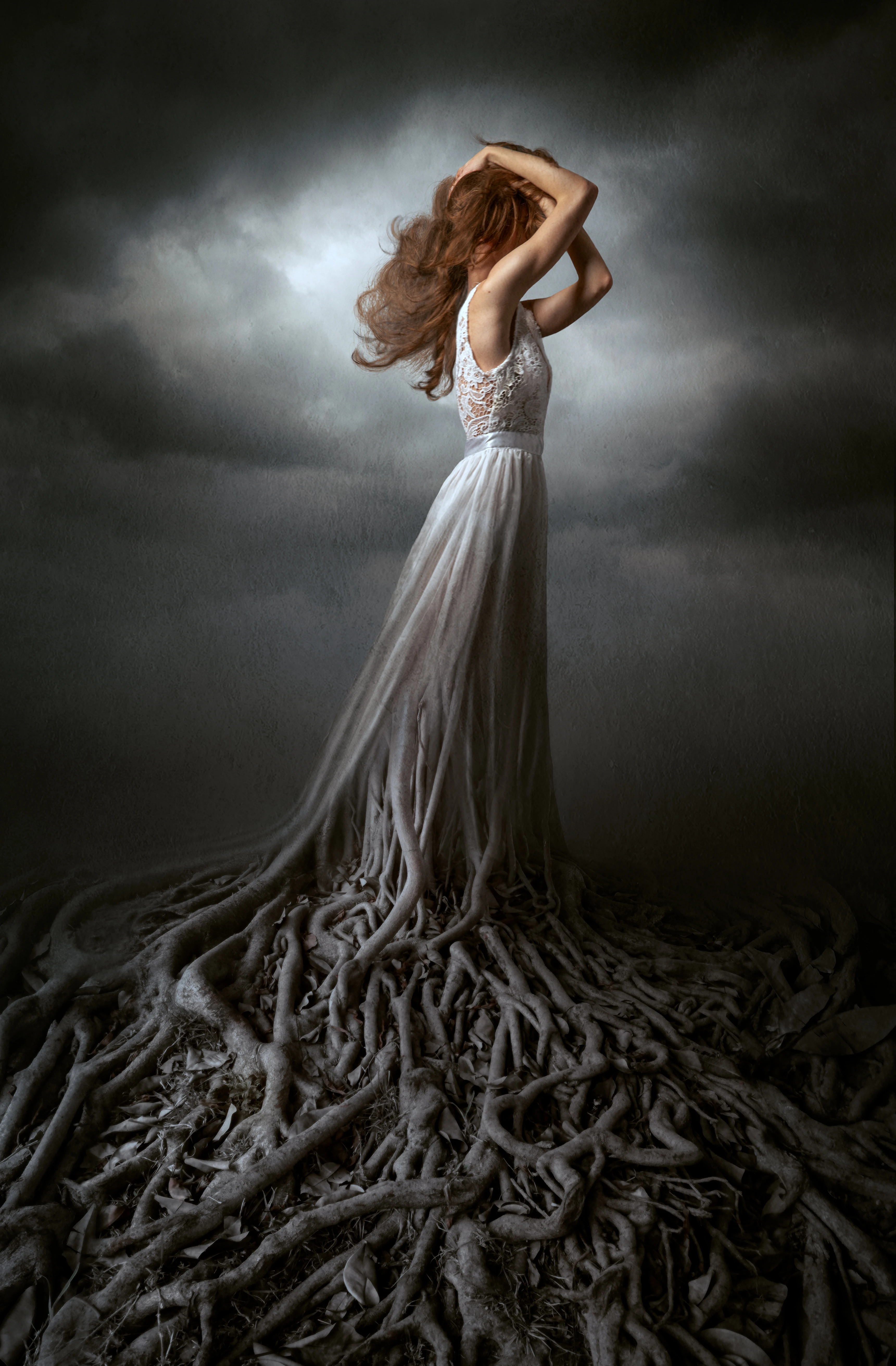 photo compositing dramatic lighting example on photo of woman in a white lace dress transforming into tree roots against a stormy sky.