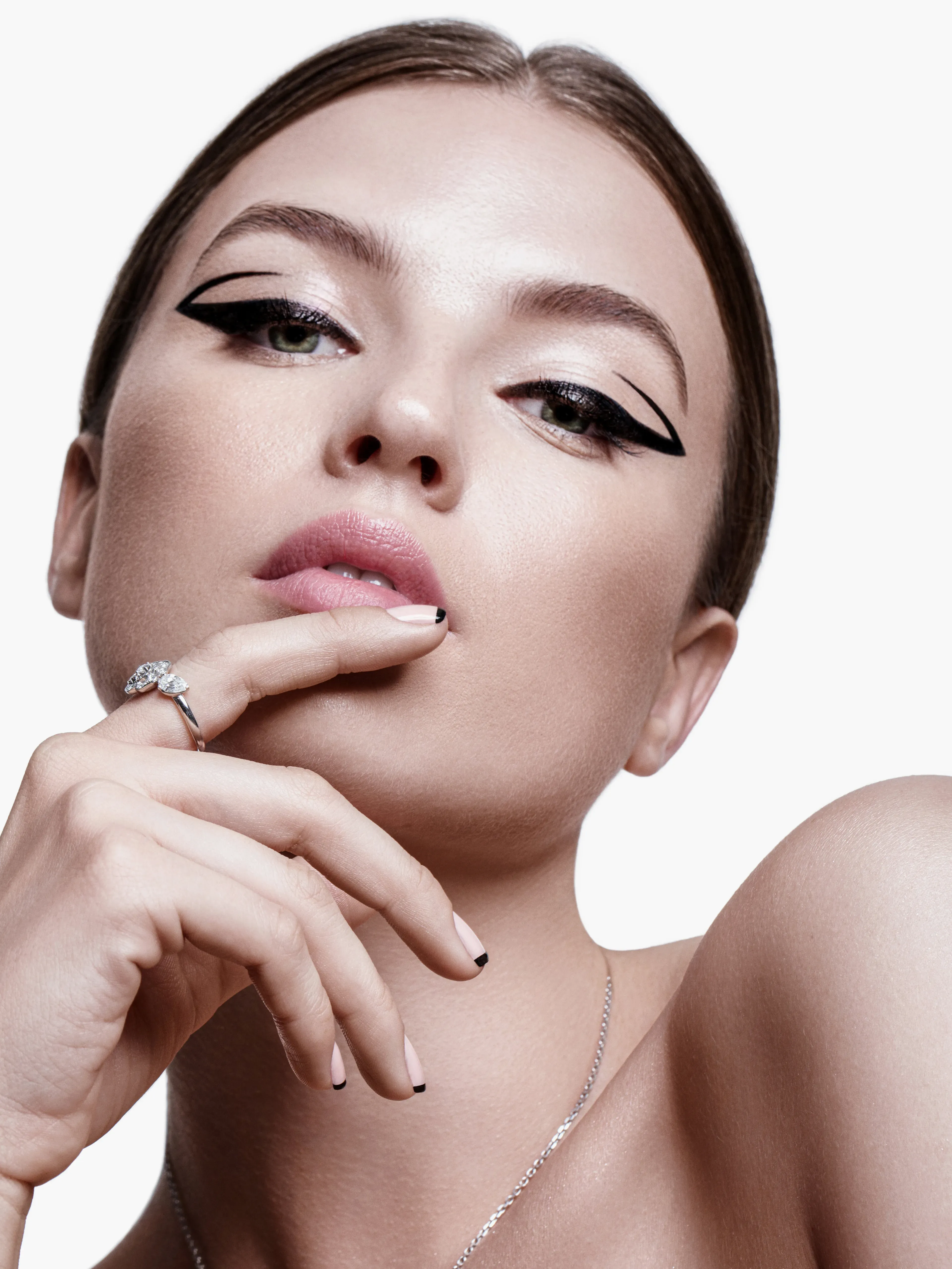 Close-up portrait with bold geometric black eyeliner, nude nails with black tips, and a silver ring.