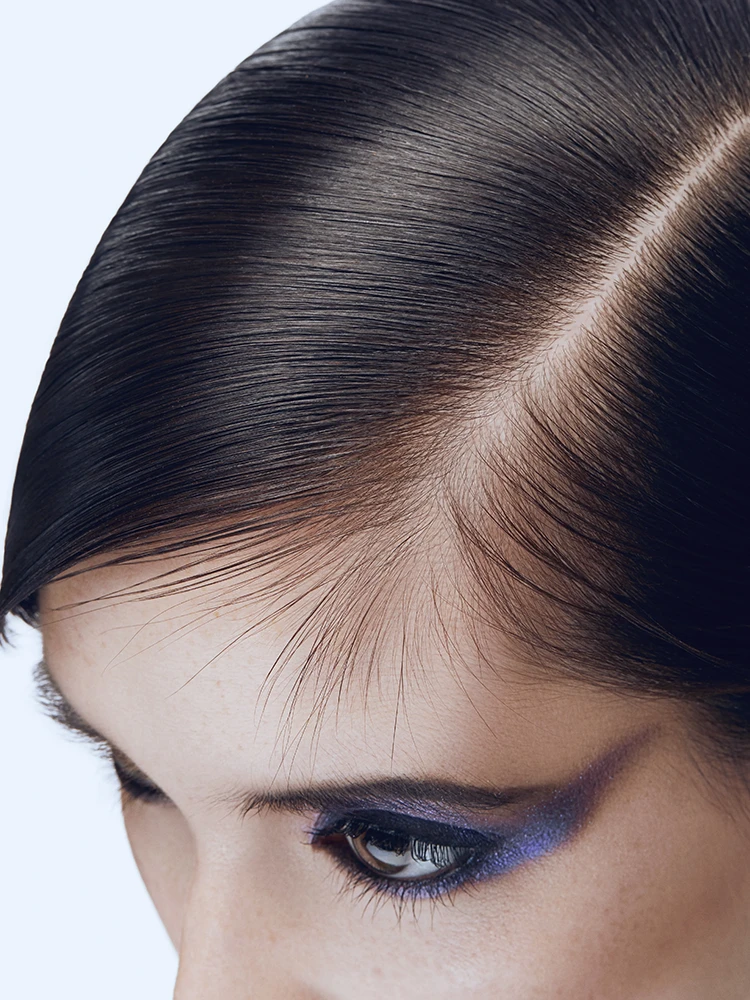 Close-up of dark hair parted cleanly with bold metallic blue and purple winged eye makeup.