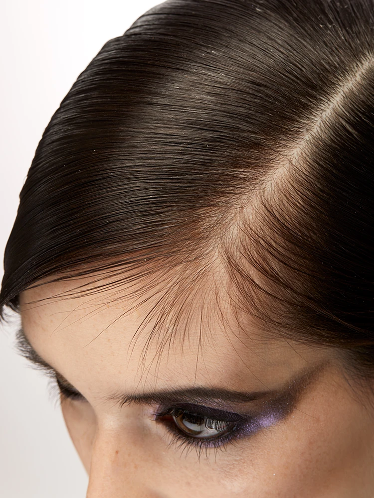 Close-up of dark hair parted cleanly with bold metallic blue and purple winged eye makeup.